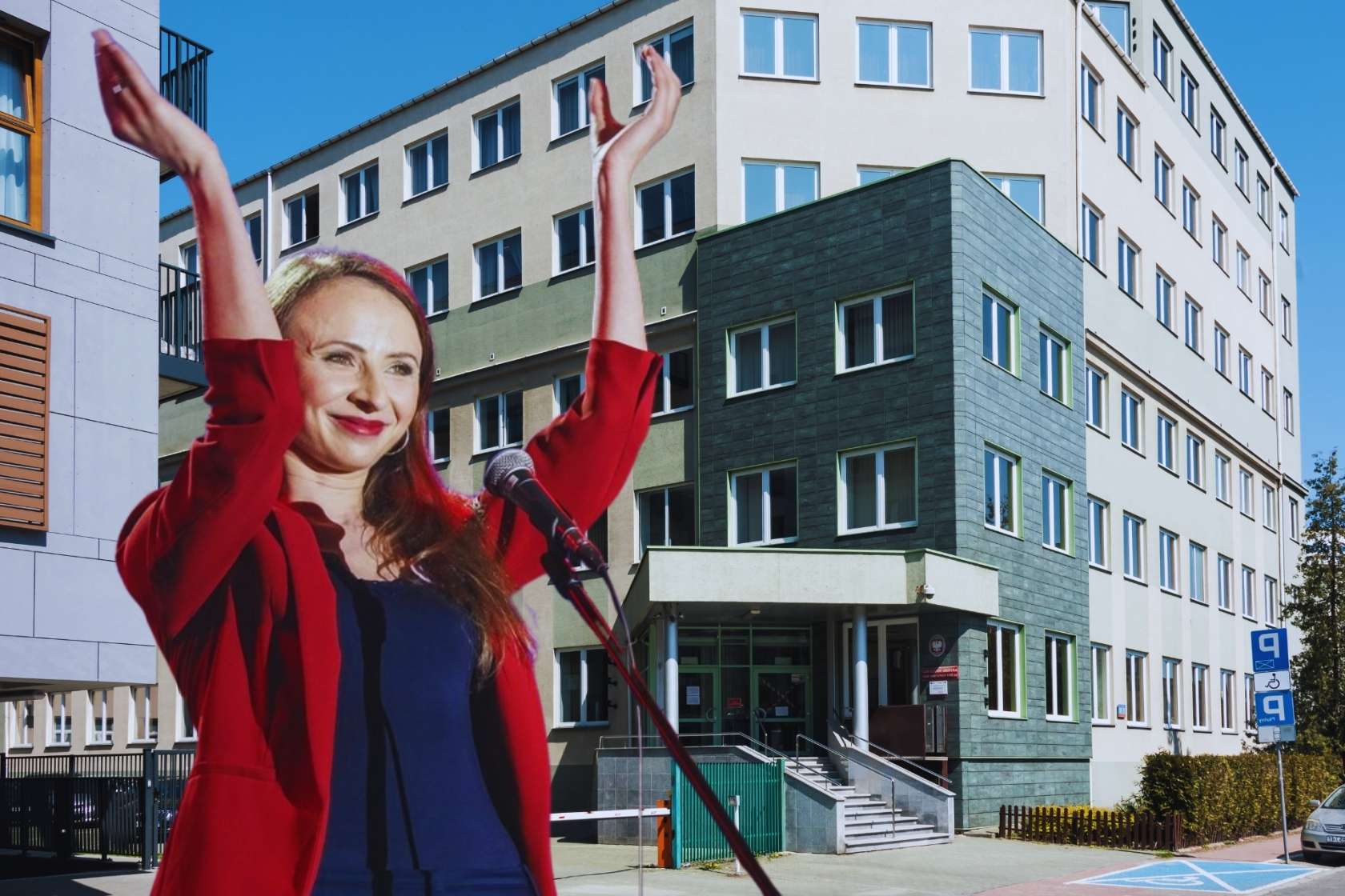 Agnieszka Dziemianowicz-Bąk w czerwonej marynarce, z uniesionymi rękami na tle budynku Państwowej Inspekcji Pracy