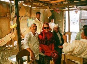 Beata Błaszczyk siedząca w hidżabie i ciemnych okularach pomiędzy jemeńskimi mężczyznami w zniszczonym pomieszczeniu w Jemenie