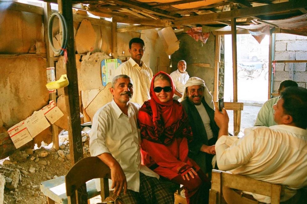 Beata Błaszczyk siedząca w hidżabie i ciemnych okularach pomiędzy jemeńskimi mężczyznami w zniszczonym pomieszczeniu w Jemenie