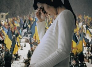 Kobieta w zaawansowanej ciąży stojąca bokiem, w tle cmentarz z mnóstwem ukraińskich flag
