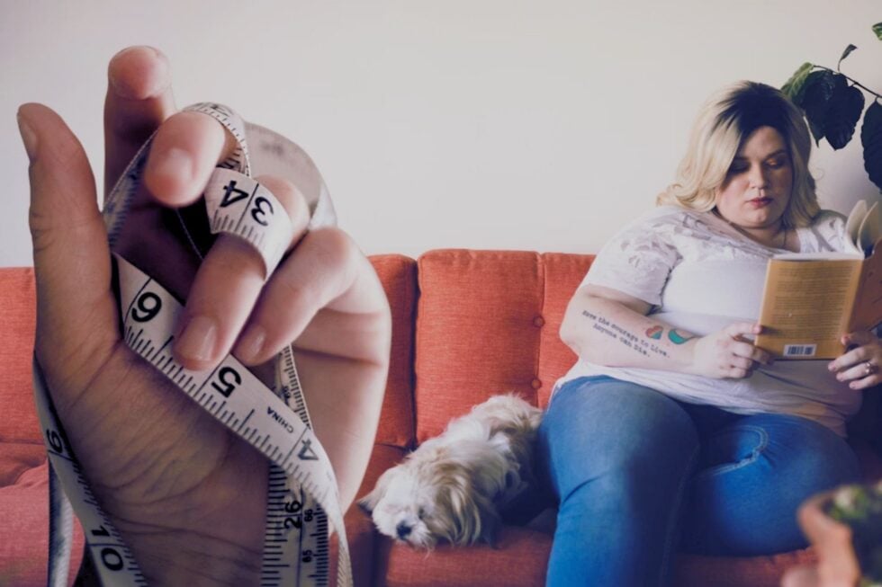 Blondynka z nadwagą czytająca książkę siedząc na kanapie, obok niej leży mały kudłaty pies, po lewej stronie doklejona jest dłoń trzymająca centymetr