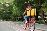 Kurier jadący na rowerze widziany od tyłu, z dużym żółtym plecakiem
