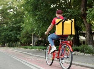 Kurier jadący na rowerze widziany od tyłu, z dużym żółtym plecakiem