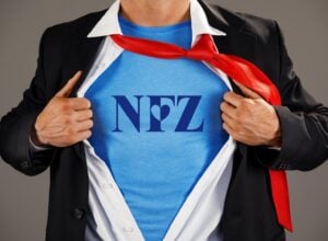 Postać superbohatera widoczna od pasa do szyi, rozchylająca koszulę i pokazująca bluzkę z napisem NFZ