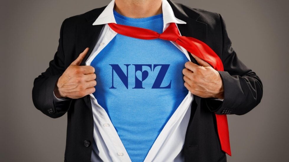 Postać superbohatera widoczna od pasa do szyi, rozchylająca koszulę i pokazująca bluzkę z napisem NFZ