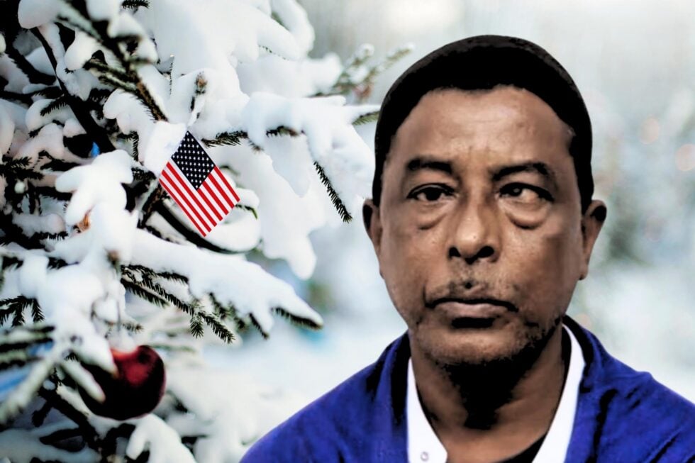 Po prawej Nurul Amin Shah Alam, mężczyzna w średnim wieku z widoczną wadą wzroku, w tle śnieg, po lewej stronie kawałek choinki z wetkniętą flagą USA