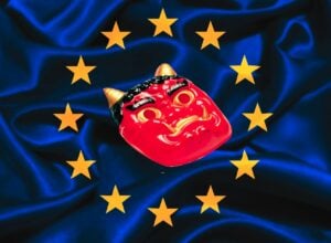 Przyciemniona flaga Unii Europejskiej, w środku między gwiazdami czerwona chińska maska przedstawiająca rogatego demona