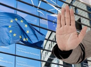 Oszklony budynek Parlamentu Europejskiego, z lewej flaga UE, z prawej dłoń pokazująca znak "stop"
