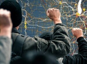 Group of people examining a large road map with many colored routes and city labels on a wall screen/board.