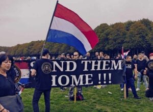Kilkadziesiąt osób z flagami Holandii, z przodu widoczny duży baner z napisem "send them home!!!"