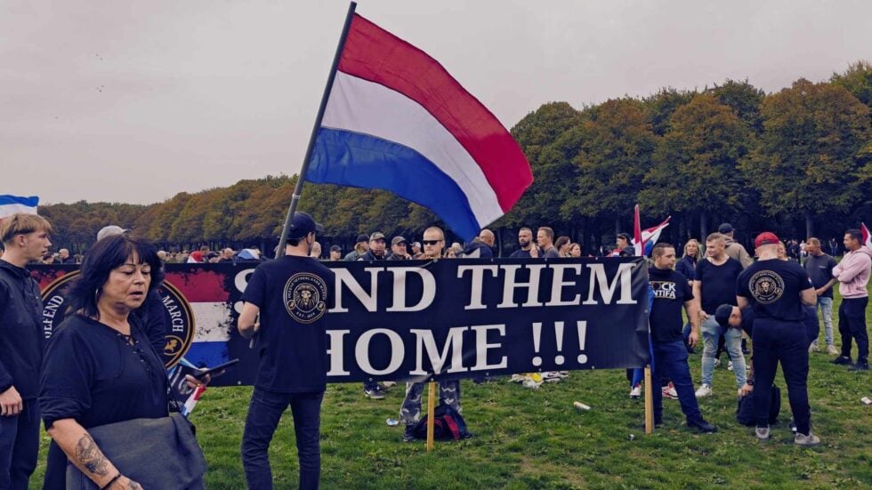 Kilkadziesiąt osób z flagami Holandii, z przodu widoczny duży baner z napisem "send them home!!!"