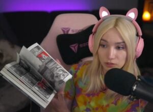Female streamer with pink cat-ear headset reading a black-and-white comic book into a microphone in a dimly lit room with purple backlighting and a pink gaming chair behind her.