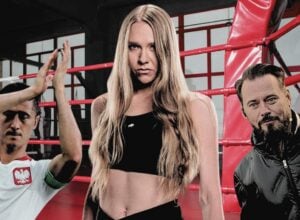 Na środku Maja Staśko (zdjęcie z materiałów prasowych High League MMA), po lewej bijący brawo Robert Lewandowski z stroju reprezentacji Polski, po prawej Krzysztof Stanowski, w tle czerwony ring boksterski