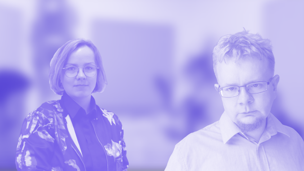 Two colleagues stand in a bright office—woman with glasses on the left, man with glasses on the right, blurred background behind them.