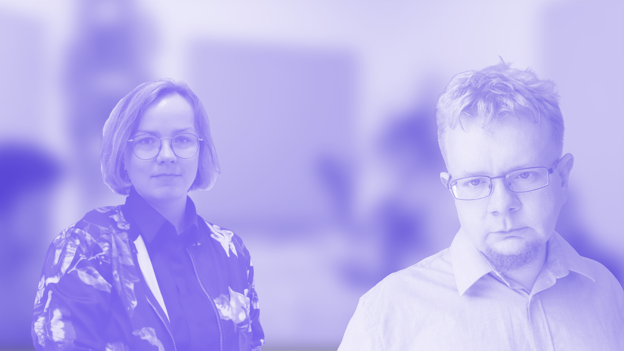 Two colleagues stand in a bright office—woman with glasses on the left, man with glasses on the right, blurred background behind them.