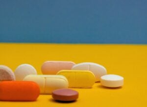 Assorted colorful pills and tablets scattered on a yellow surface with a blue wall in the background.
