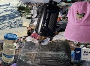 Na tle wysypiska śmieci: sweterek w krowy, e-papieros, fiolki z lekami, tajemnicza paczka zawinięta folią, różowa kaszkietówka z haftem kury, opakowanie Xanaxu