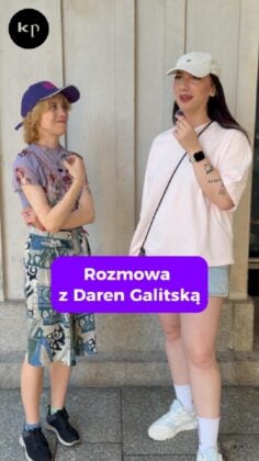 Two women stand outside, one in a purple cap and patterned skirt, the other in a white cap and pink shirt holding a microphone. A purple banner reads 'Rozmowa z Daren Galitską'.