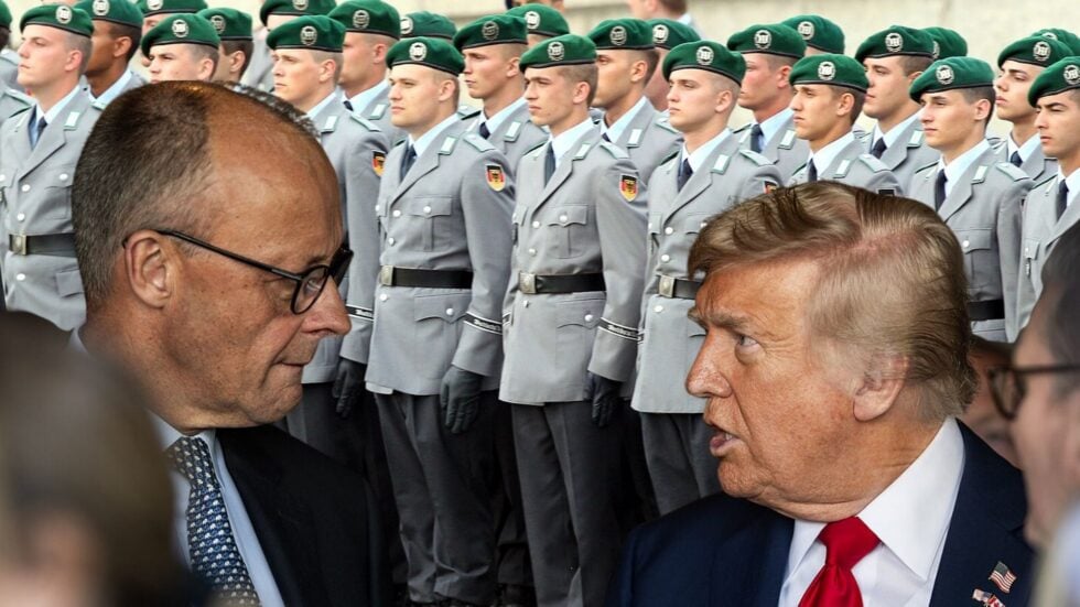 Two men in suits conversing in the foreground with a line of uniformed soldiers in gray uniforms and green berets behind them