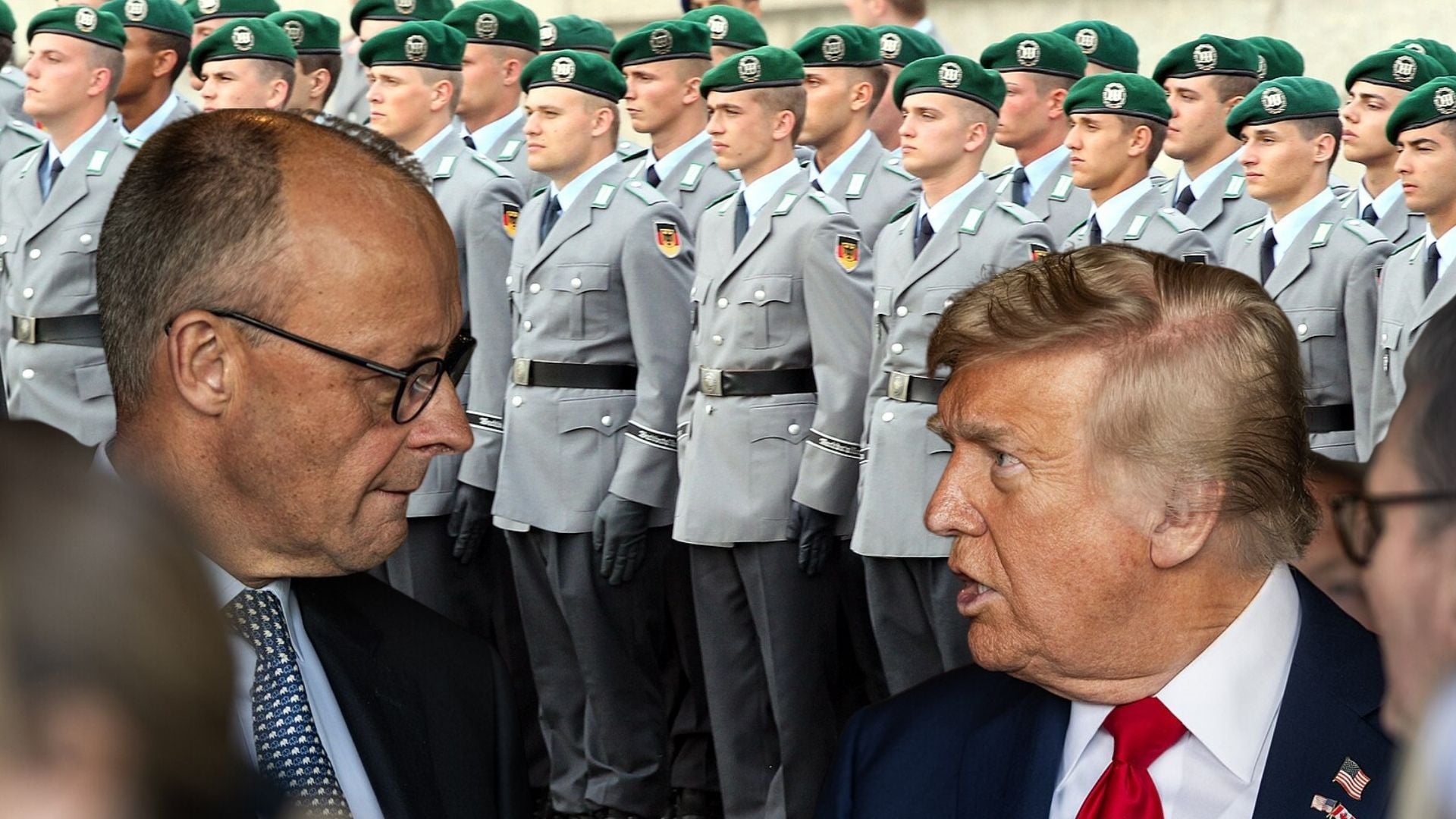 Two men in suits conversing in the foreground with a line of uniformed soldiers in gray uniforms and green berets behind them
