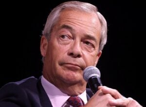 Close-up of a gray-haired man in a suit speaking into a handheld microphone on stage.