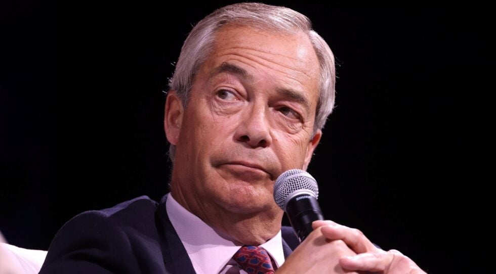 Close-up of a gray-haired man in a suit speaking into a handheld microphone on stage.