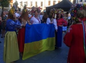 Group of people in traditional Ukrainian dress holding a large blue-and-yellow flag at a festive street event.