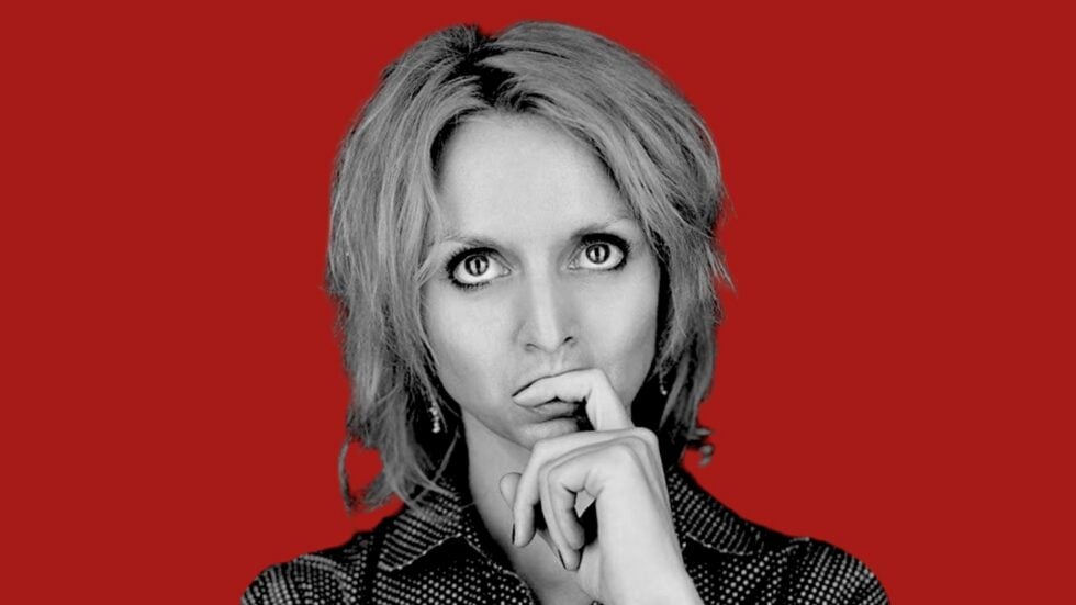 Portrait of a woman in black-and-white, with a contemplative pose and hands near her mouth against a red background.