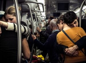 A couple shares a tight hug in a crowded subway car, standing beside metal poles and holding on for support.