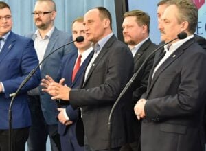 Group of men in business suits at a press conference, speaking into microphones.