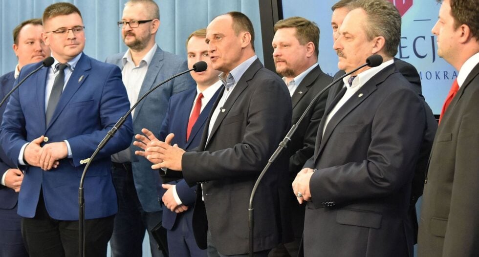 Group of men in business suits at a press conference, speaking into microphones.