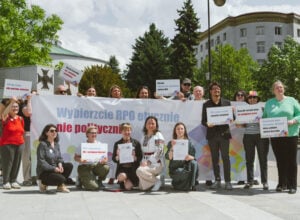 Group of diverse protesters holding placards and a large banner in a city square.