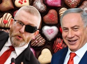 Two men in suits with red ties leaning toward the camera, one wearing an eye patch, smiles with a background of heart-shaped chocolates.