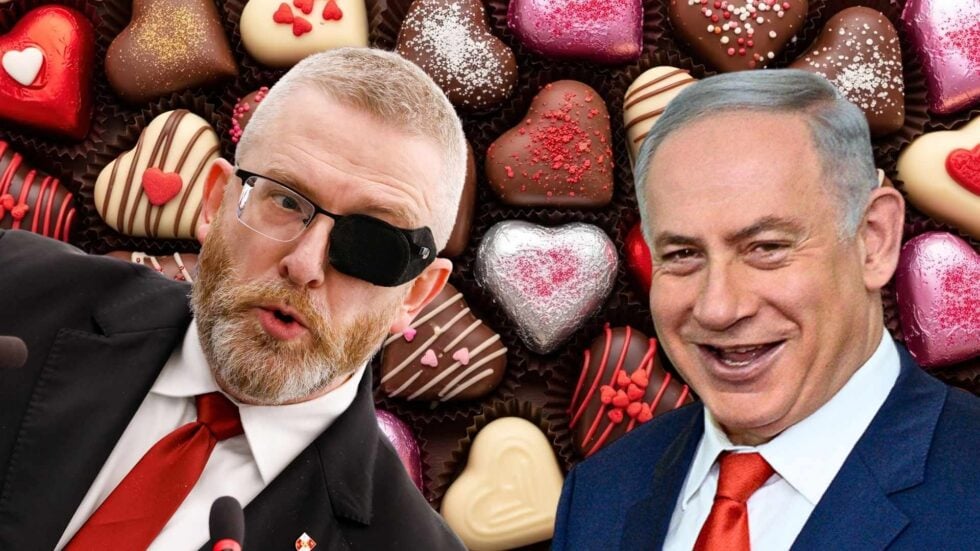 Two men in suits with red ties leaning toward the camera, one wearing an eye patch, smiles with a background of heart-shaped chocolates.