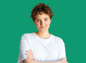 Portrait of a young woman with short curly hair, wearing a white T‑shirt, arms crossed, against a teal background.