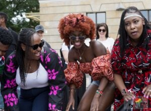 A group of diverse friends in colorful outfits smiling and posing outdoors at a festival ground.