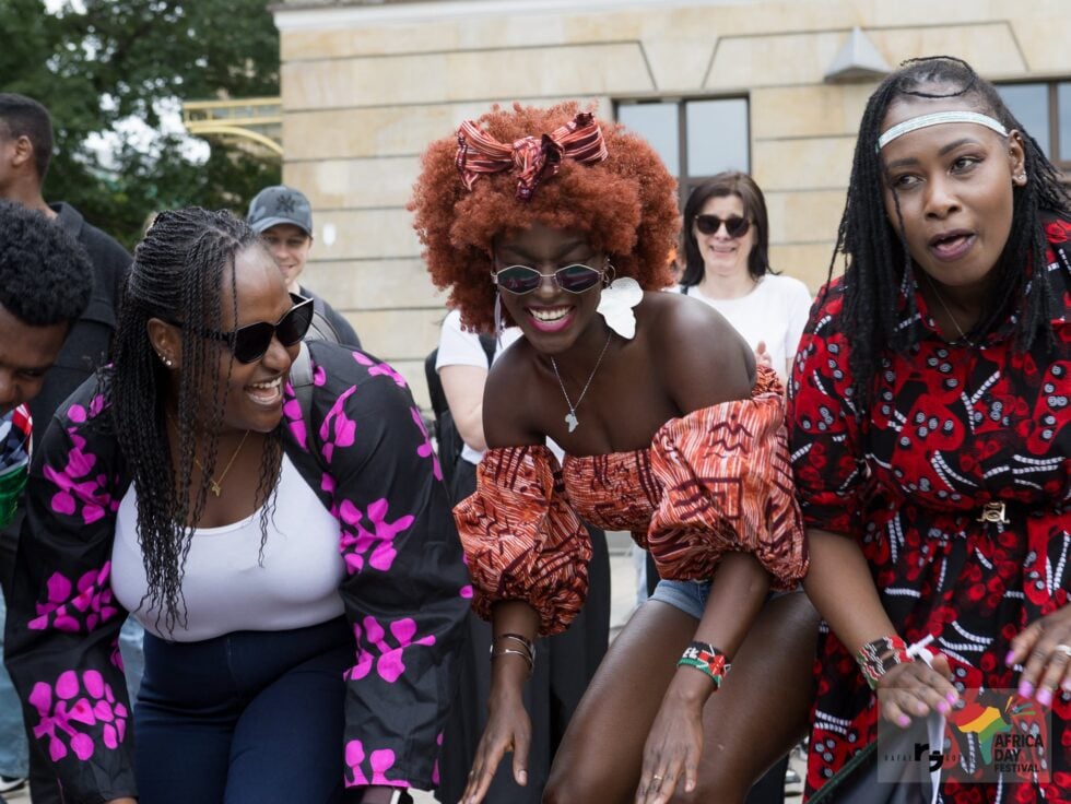 A group of diverse friends in colorful outfits smiling and posing outdoors at a festival ground.