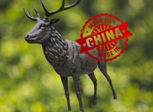 Olsztyński pomnik jelenia na zielonym leśnym tle, na nim duża czerwona plakietka "made in China"