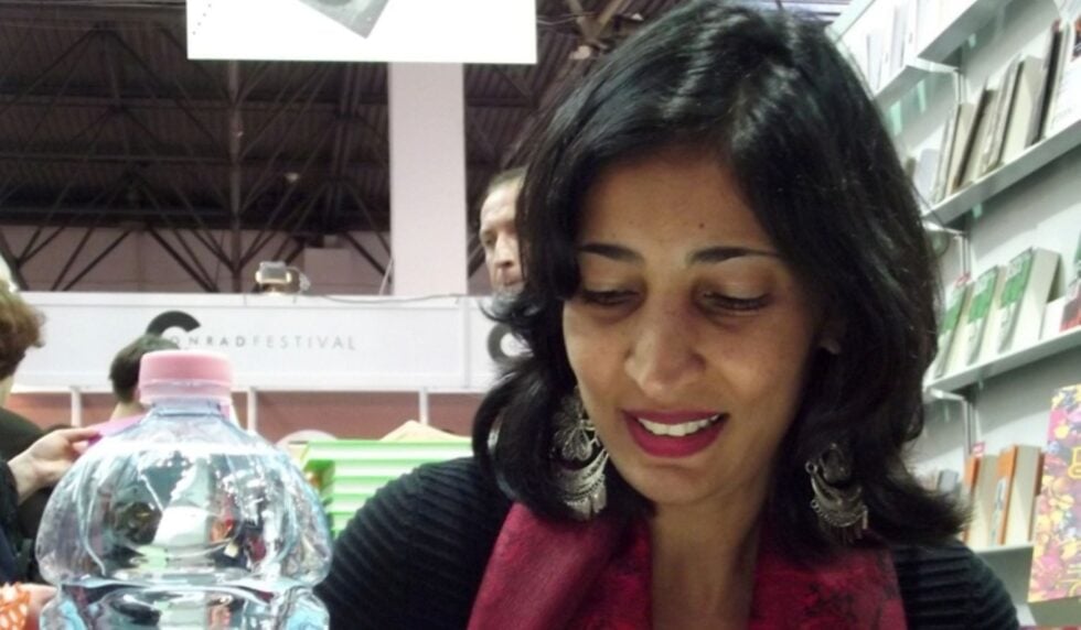 Woman with dark hair and red scarf smiling in a bookstore, shelves of books behind her and a glass globe in the foreground.