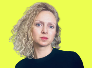 Portrait of a woman with curly blonde hair wearing a black top, looking to the right, against a bright yellow background.