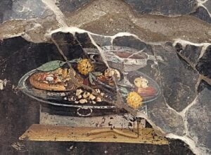 Fragment of a weathered religious painting embedded in a cracked stone wall, with dried yellow flowers nearby.