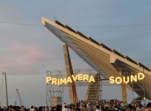 Outdoor Primavera Sound festival entrance with illuminated letters on scaffolding and a crowd gathered beneath.