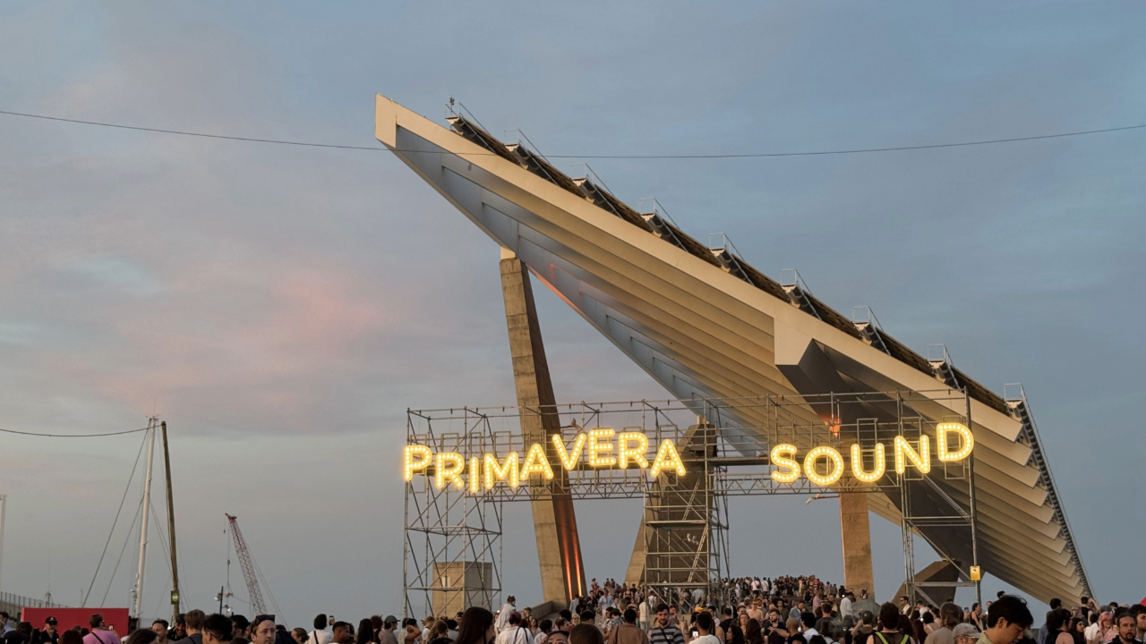 Outdoor Primavera Sound festival entrance with illuminated letters on scaffolding and a crowd gathered beneath.