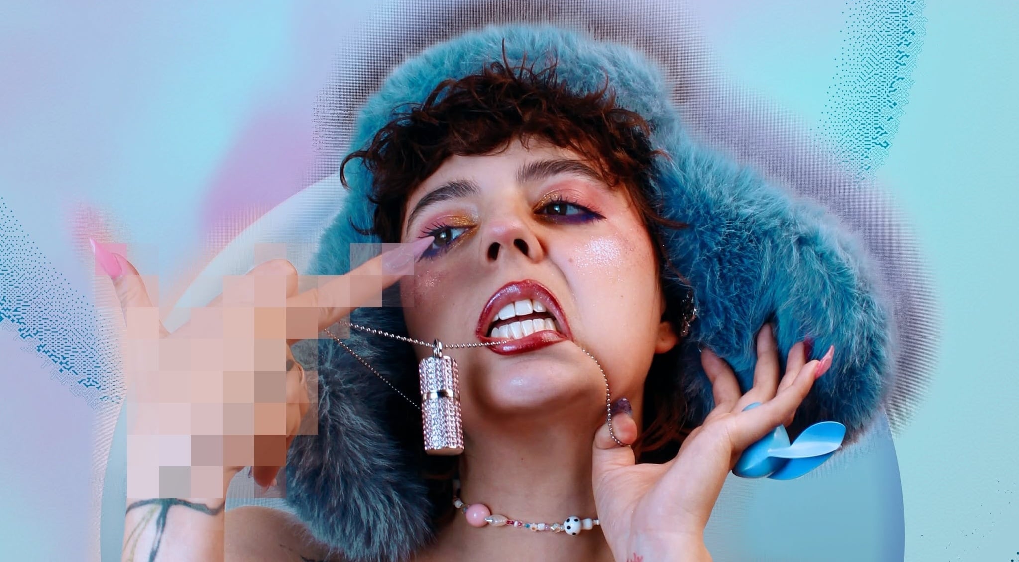 Close-up portrait of a person with a blue faux-fur hood, bold makeup, biting a silver pendant necklace while touching their face.