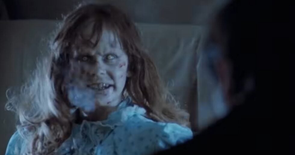 Pale zombie woman with a blood-streaked face and ragged hair in a tattered blue dress, in a dark scene.