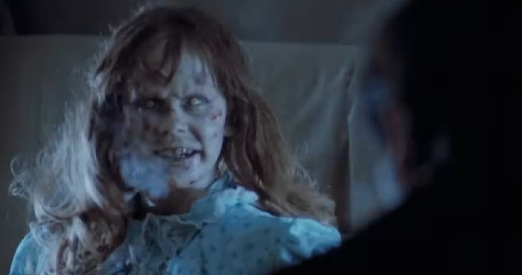 Pale zombie woman with a blood-streaked face and ragged hair in a tattered blue dress, in a dark scene.