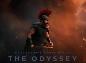 Promotional poster featuring a armored warrior with a red crest helmet shouting amid orange smoke and embers, linking to a Christopher Nolan film The Odyssey.