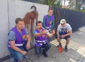 Four volunteers in purple safety vests posing with thumbs up beside a concrete wall with a brown horse mural.