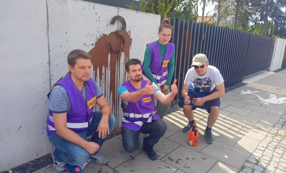 Four volunteers in purple safety vests posing with thumbs up beside a concrete wall with a brown horse mural.