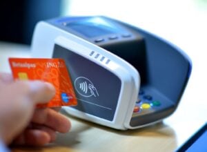 Close-up of a hand tapping an orange card against a card reader for contactless payment.